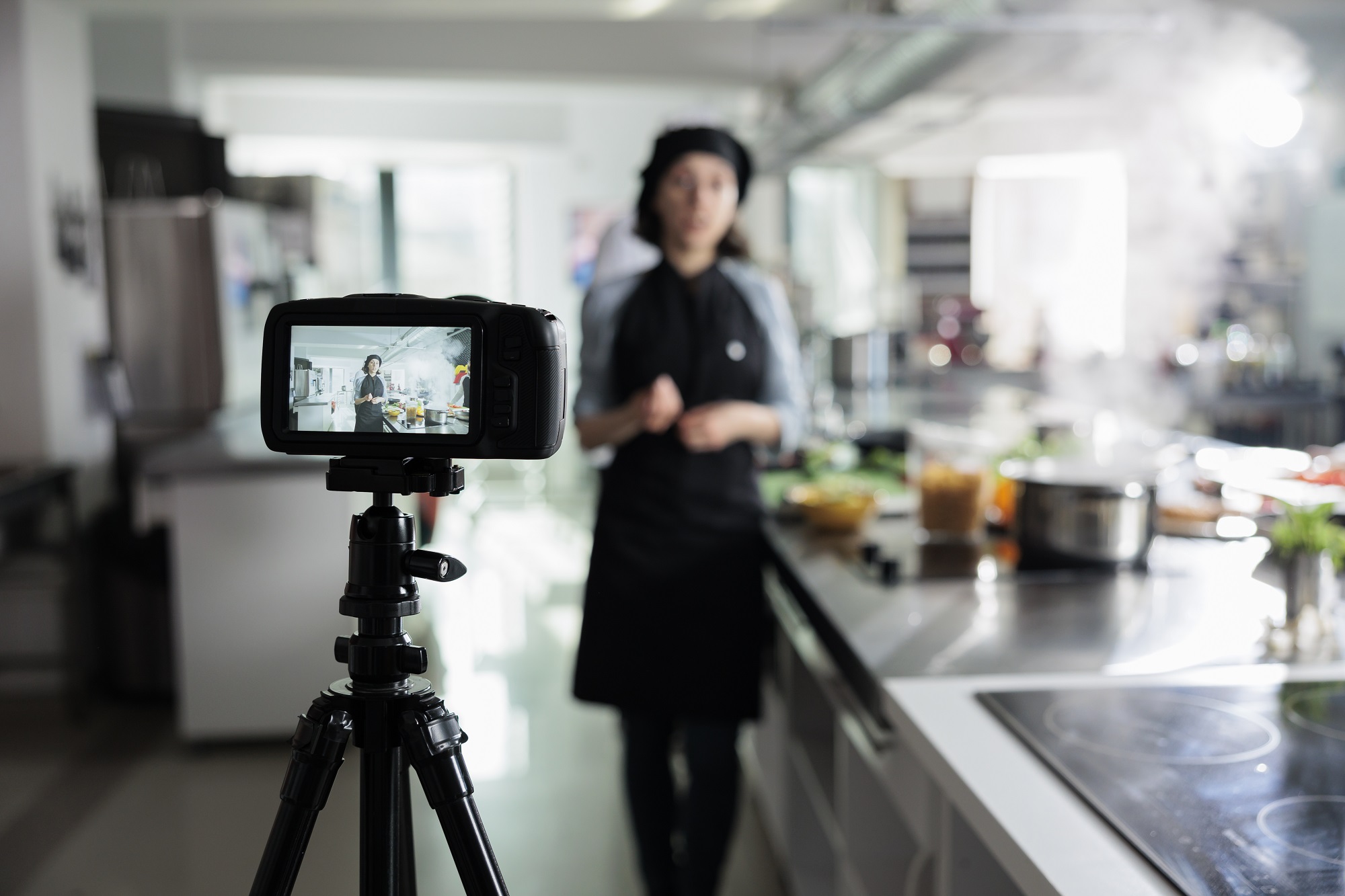 Confident cook shooting a culinary vlog for online platform and television program. Head chef smiling heartily in front of camera while filming a cooking course in restaurant professional kitchen.